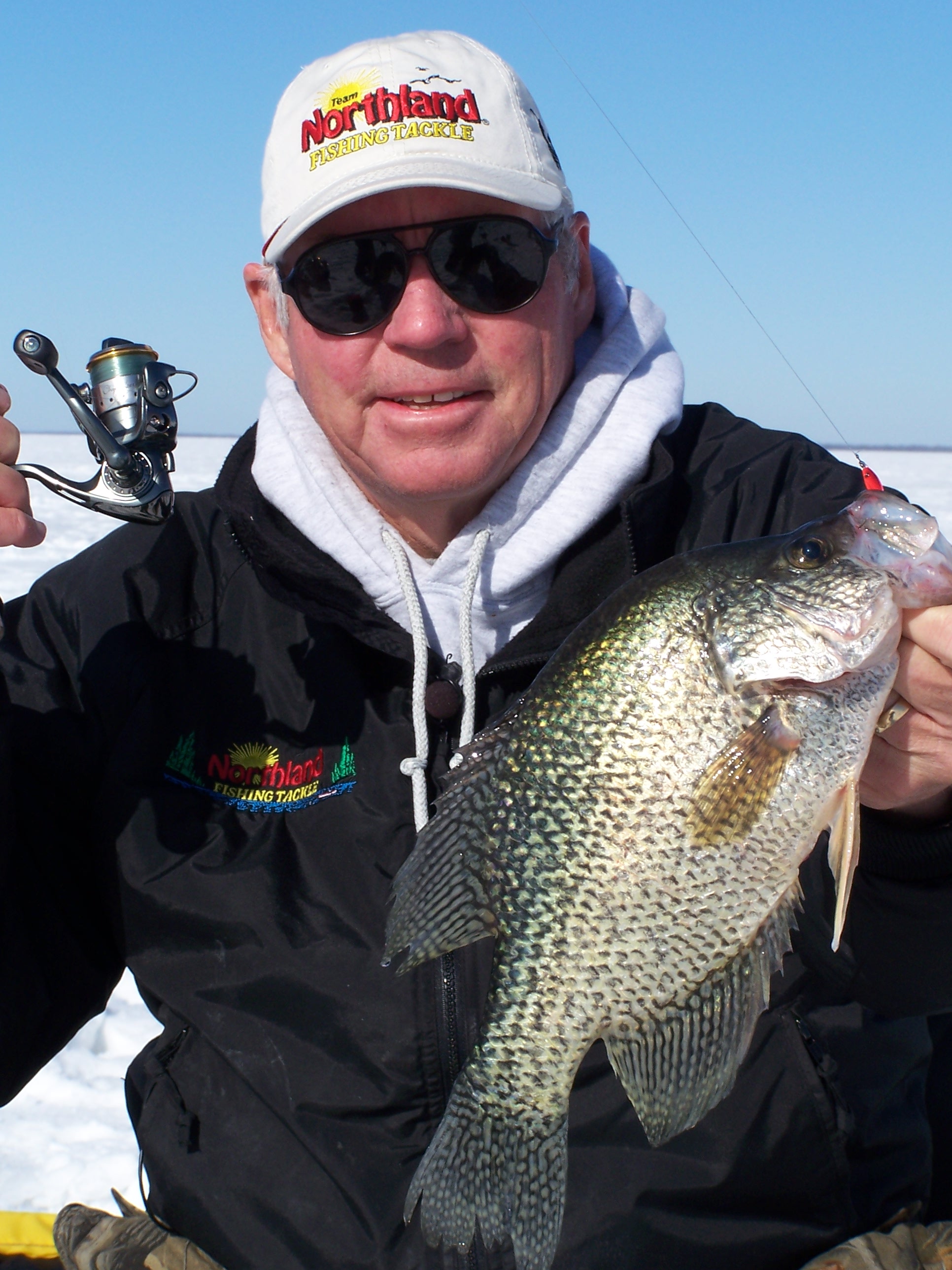 An ice fisherman showing off a crappie that he caught.
