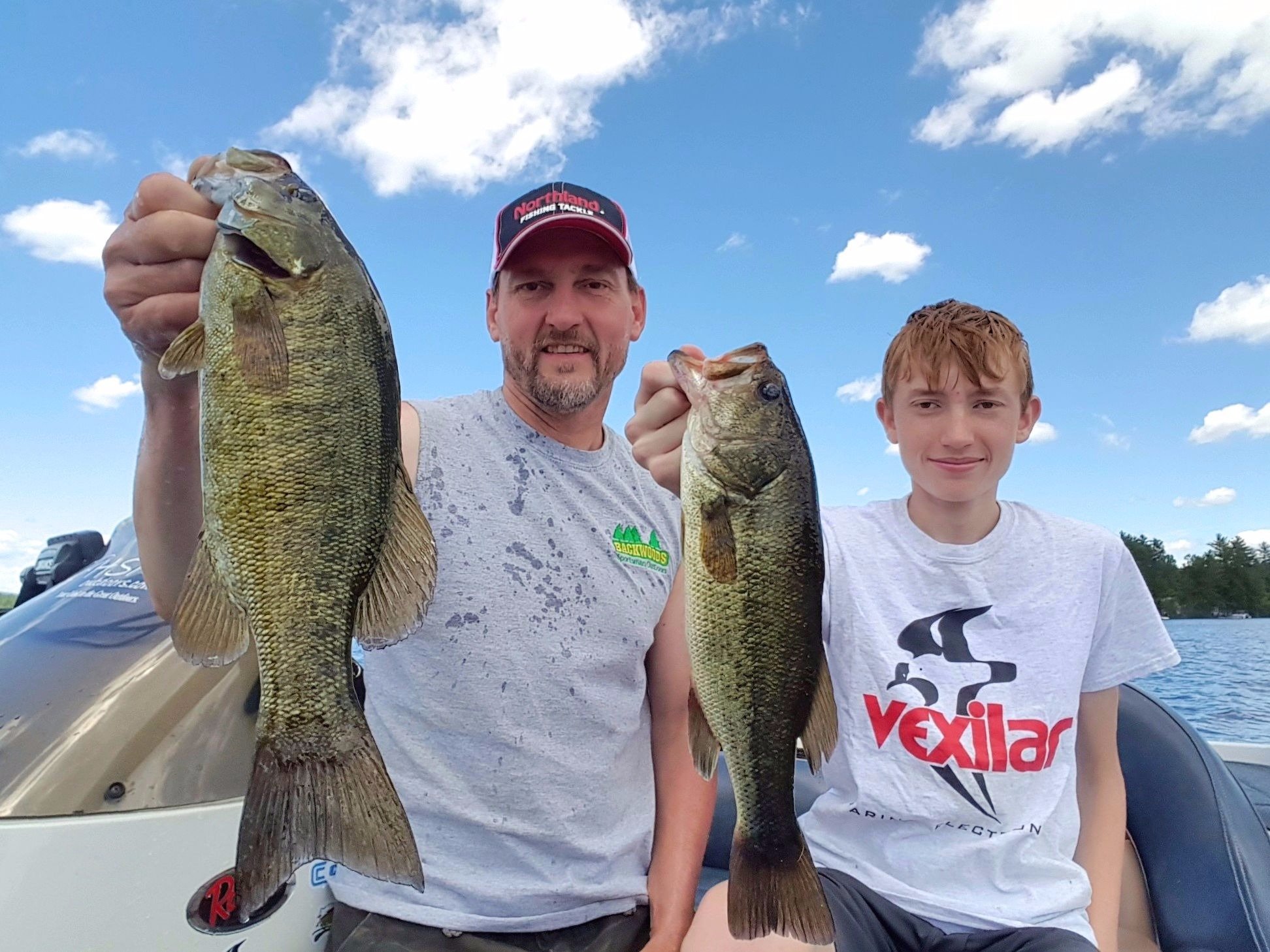 A father and son with a largemouth and smallmouth bass they caught.