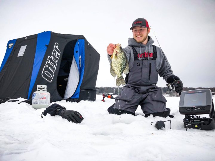 Angler ice fishing and holding up a crappie he caught.