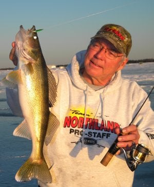 An ice fisherman holding up a walleye he caught on a spoon.