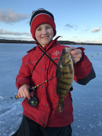 Young ice fisherman holding up a perch he caught