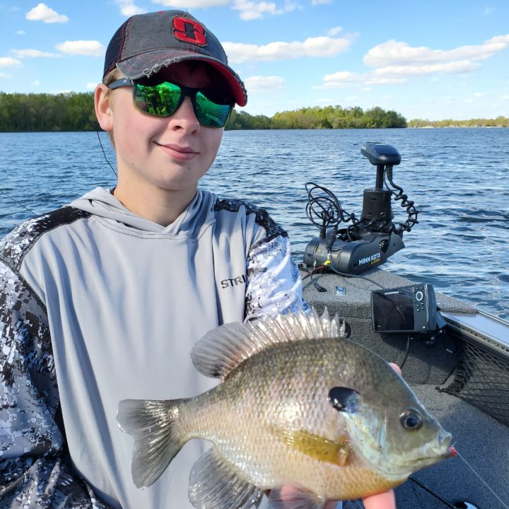 A young fisherman holding up a bluegill he caught fishing.