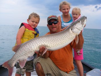 Angler hiolding a muskie he caught with his three kids