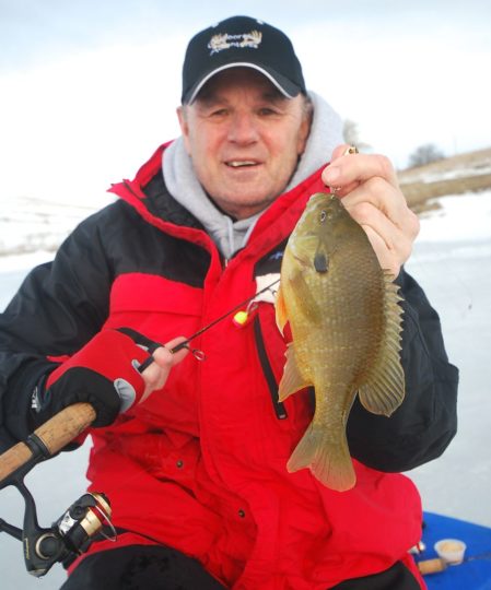 An ice fisherman showing off a bluegill he caught.