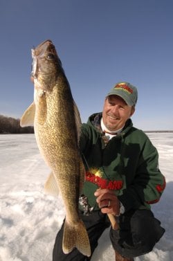 An ice fisherman holding up a big walleye he caught while ice fishing.
