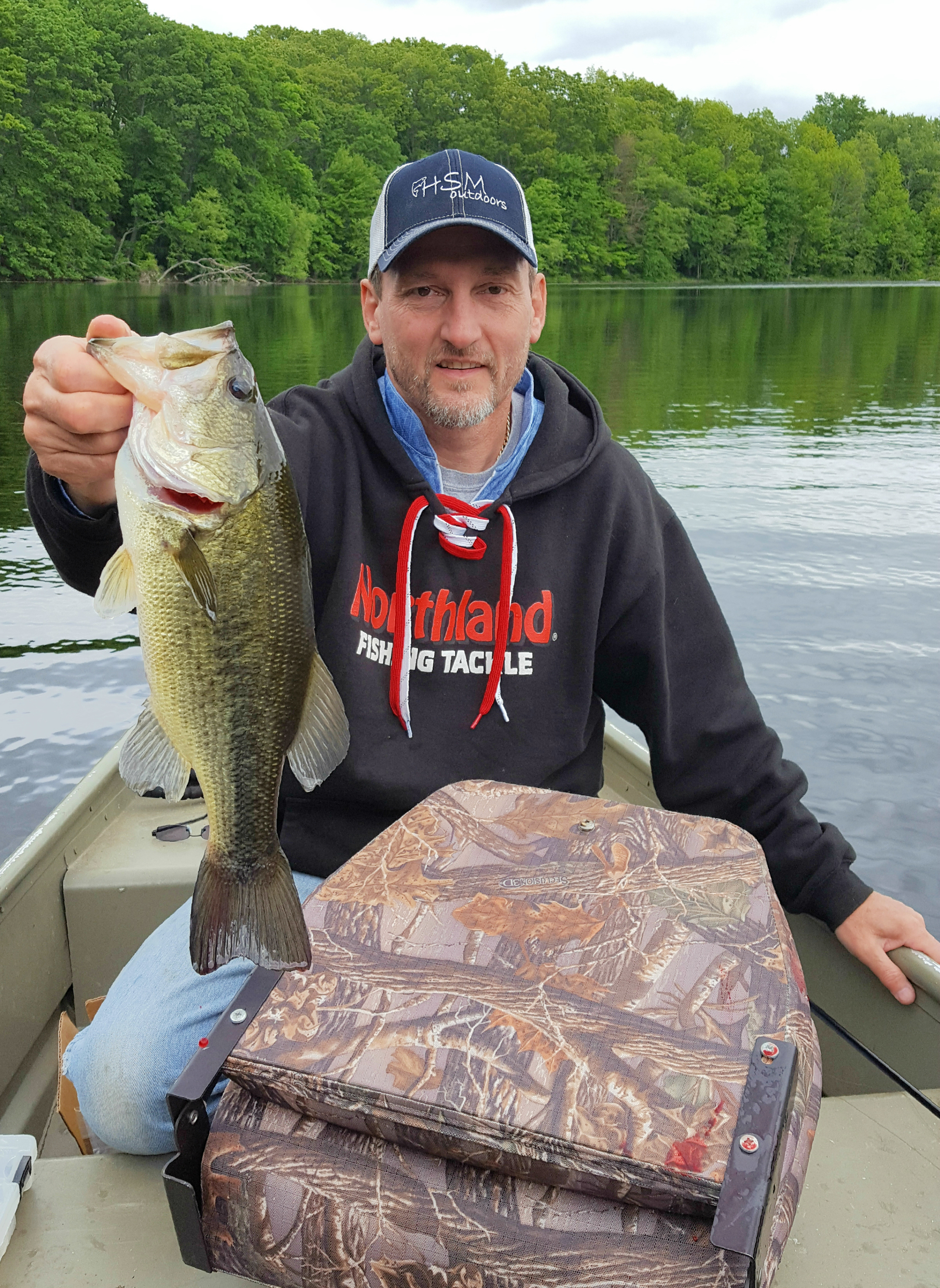 Fisherman holding up a largemouth bass he caught fishing in a pond.